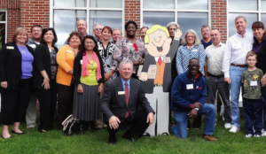 A group of people, including Bill and Little Bill of Coffee News, posing for a group photo. Little Bill is a life size 2 dimensional cartoon display.