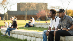 Grand Valley State University students sitting along a stone wall landscaping.