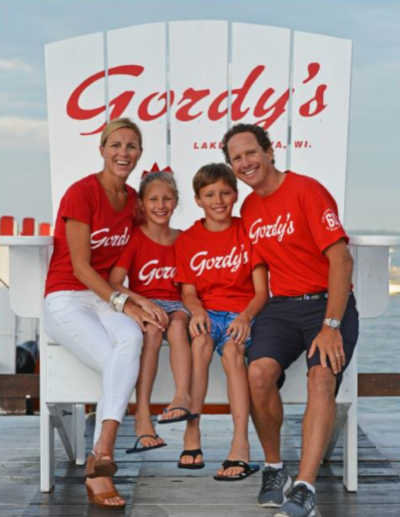Gordy's Lakefront Marine, a family of 4 sits on a large white wooden Gordy's chair to pose for a photo.