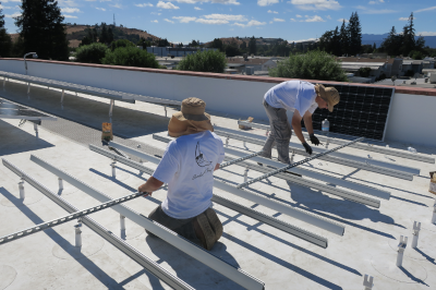Two men working on a roof to install solar panels on a metal framework they are creating.