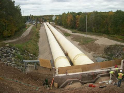 Two long steel pipes going down the center of the photo into the distance. Trees and paths on the left and right.